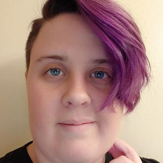 A white nonbinary person with blue eyes and short purple hair.